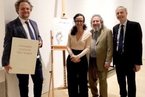A group of people pose around an art piece on an easel, one of the people holds a large book