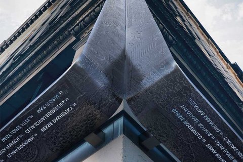 Curved metal memorial with engraved text mounted on the corner of a historic building