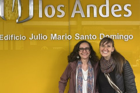 Two women pose in fornof a sign for the "Universidad de los Andes"