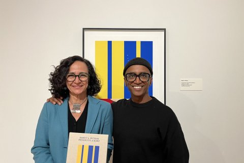 Two people pose in front of framed art piece in a gallery