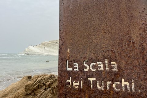 White cliffs along the ocean with a rusted piece of  metal with the words "La Scala dei Turchi" in the foreground