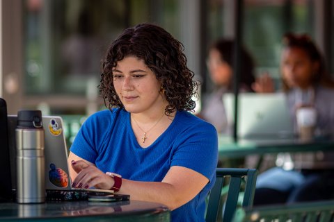 Student working on their laptop outside in a cafe patio.