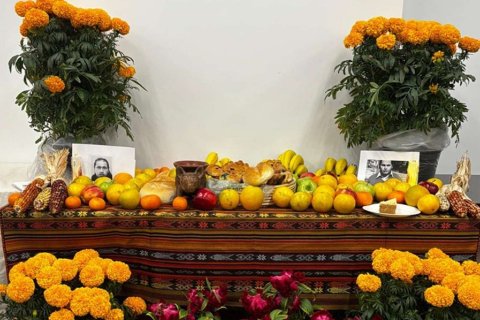 Día de los Muertos altar decorated with orange marigolds, fruit, bread, corn, photographs, and other offerings arranged on a colorful woven cloth
