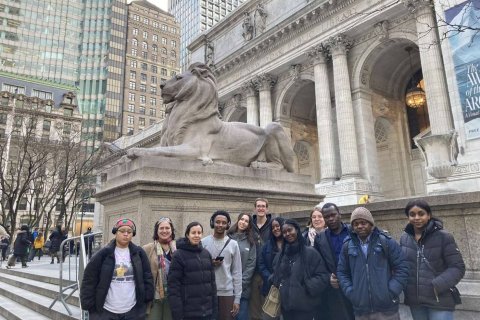 A group of college students pose in front of the Lion Statues in front of the New York Public Library