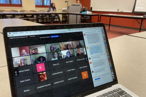 A laptop sits on a table and a Zoom call displays on the screen