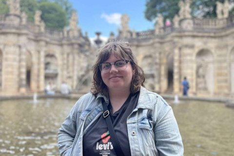 A woman stands outside in front of an ornate stone fountain