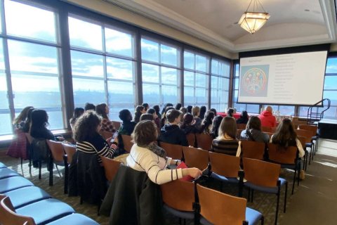 A group of people sit in a conference room and watch a presentation