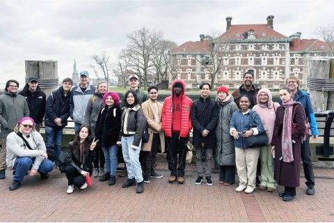 A group of college students and professors pose in front of Ellis Island