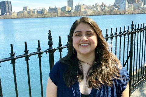 A woman stands in front of a wrought iron fence in front of a lake