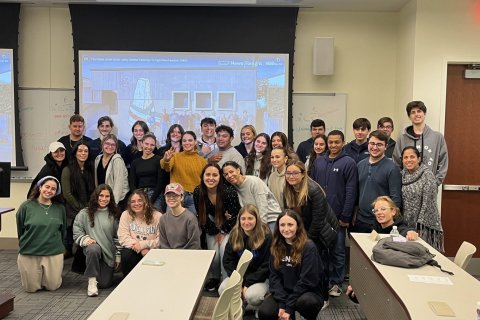 A group of college students pose in a classroom in front of a projector screen