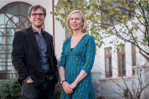 Two adults pose for a headshot outside in front of a building