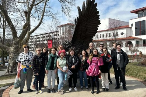 A group of college students pose together in front of a metal statue of a Red Hawk