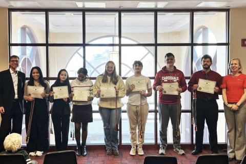 A group of college students stand in a line holding paper certificates