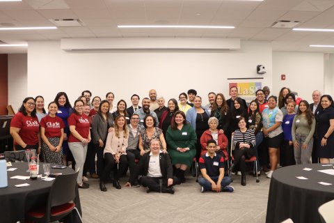 A group of people pose inside a conference room, a few wear t-shirts that read "Clase"