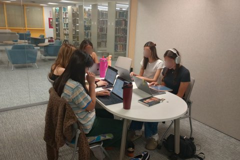 5 students sitting at a table on laptops inside a study pod