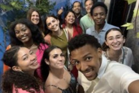 A college student holds a phone and takes a selfie with a group of other college students