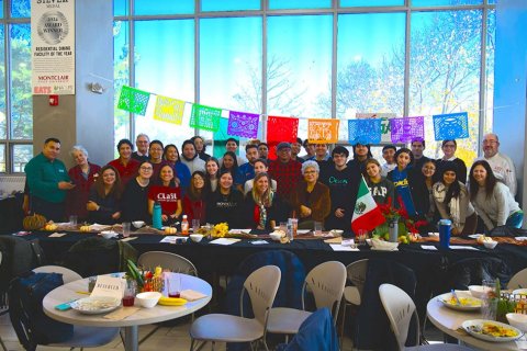 A large group of people pose together in a room with large windows and colorful flags
