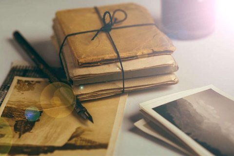 A stack of aged letters tied with string rests beside a fountain pen and scattered vintage photographs on a softly lit desk
