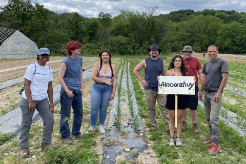 A group of people stand in the middle of a crop field while one holds a sign