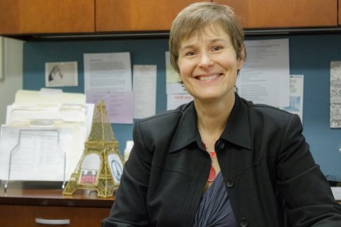 A woman poses in an office, a sculpture of the Eiffel Tower stands on the desk behind her