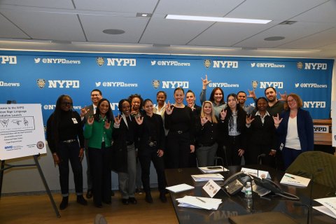 A group of people pose inside a conference room in front of a banner with the NYPD logo