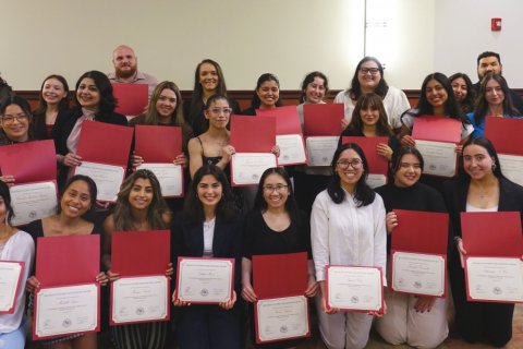 A gorup of people pose together each holding a certificate inside a holder