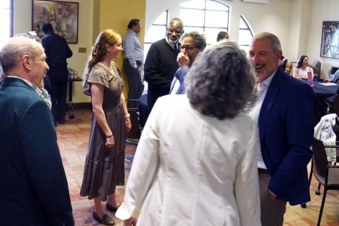 A gorup of people in professional attire mingle inside a conference room