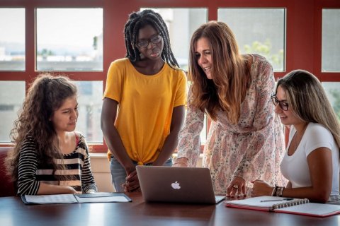 A college professor stands over a laptop and types while three students watch