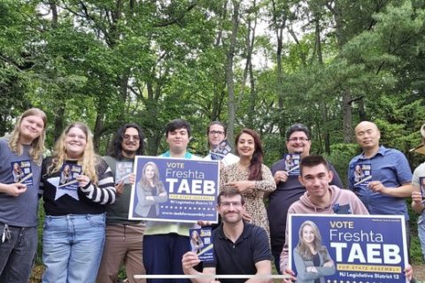 A group of people stand together holding signs reading "Vote Freshta Taeb"