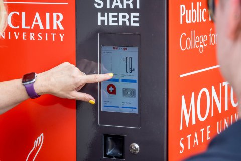 A hand points to a digital keypad on the Harm Reduction Kiosk.