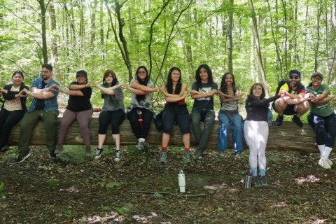 photo of field school students sitting on a fallen tree log, interlocking arms and using hands to make hearts