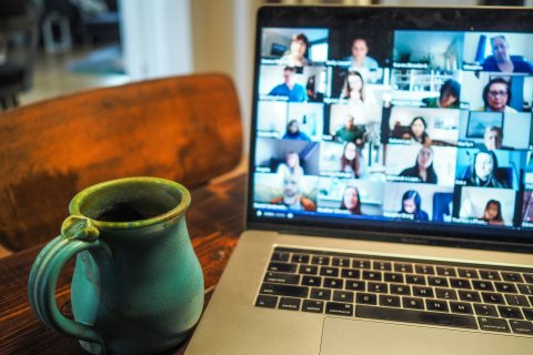 A coffee cup sits next to a laptop open with Zoom participants. 