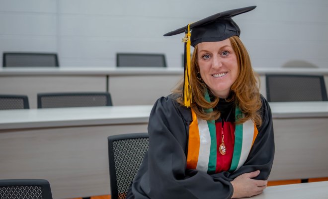 Jean-Marie Beeks sits in a classroom in her graduation cap and gown.