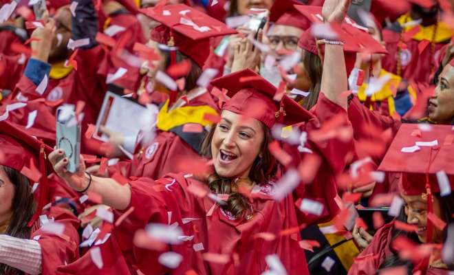 graduate holds cell phone to take selfie amid a flurry of confetti