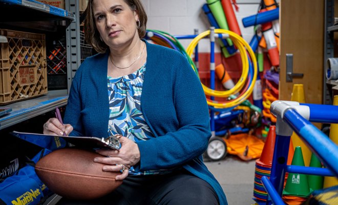 Kinesiology Professor Melissa Alexander is seated, holding a clipboard and football.