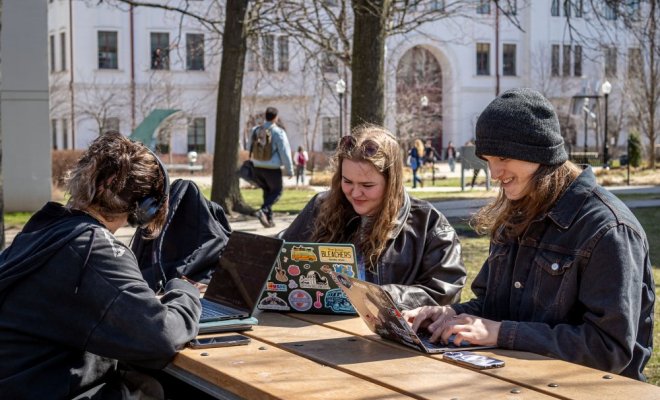 Students sitting outdoors on campus working on their laptops.