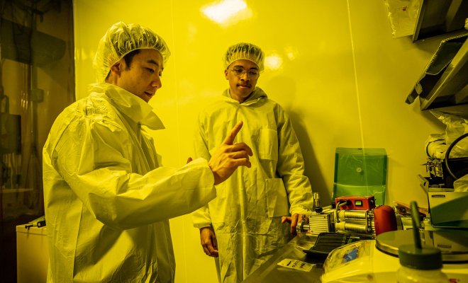 Two men in lab coats under the yellow light of the lab.
