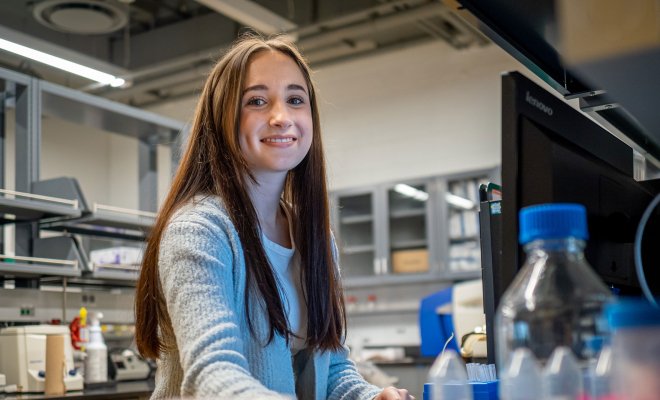 A female student smiles at a computer in a science lab.