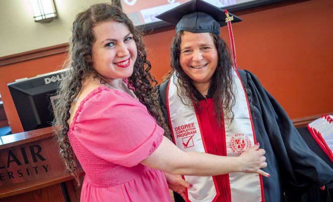 A young woman adjusts her mother's graduation stole.