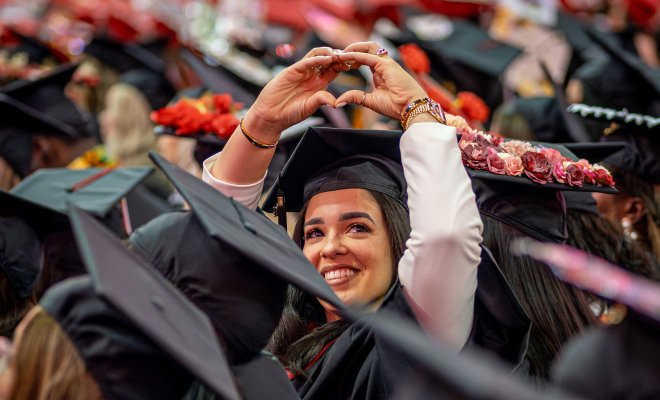 A graduate smiles and holds up their hands in the shape of a heart