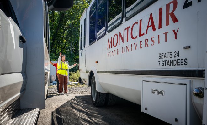 Woman in between two Montclair University buses signaling. 