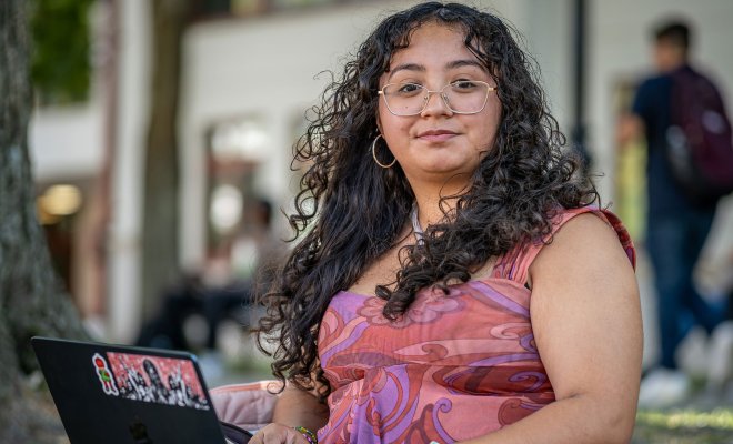 Sara Flores sitting on campus with her laptop open.