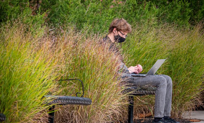 Male sitting outside on a bench, wearing a mask