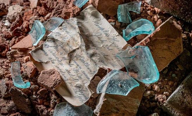 Handwritten message surrounded by glass pieces from broken bottle laid on bricks