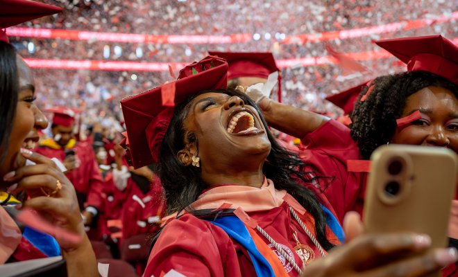 master's graduate student in red cap and gown smiling with confetti falling around them