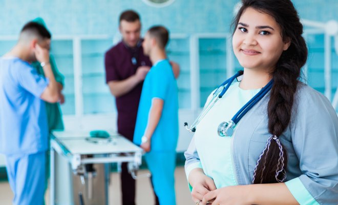 Woman in medical attire, stethoscope around her neck and her colleauges in the background.