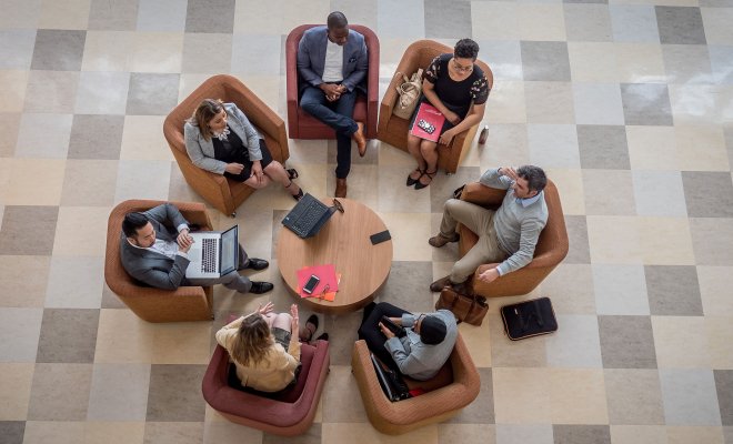 Seven graduate students collaborating while seated in a circle with laptops and papers