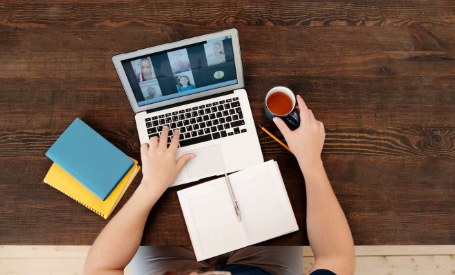 person sitting at computer with open notebook and a tea
