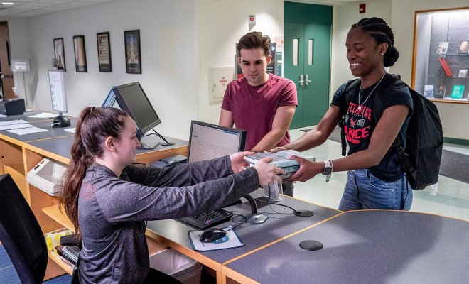 students checking out a book at front desk