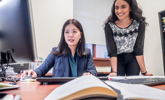 Academic advisor advising a student standing beside her behind a desk.